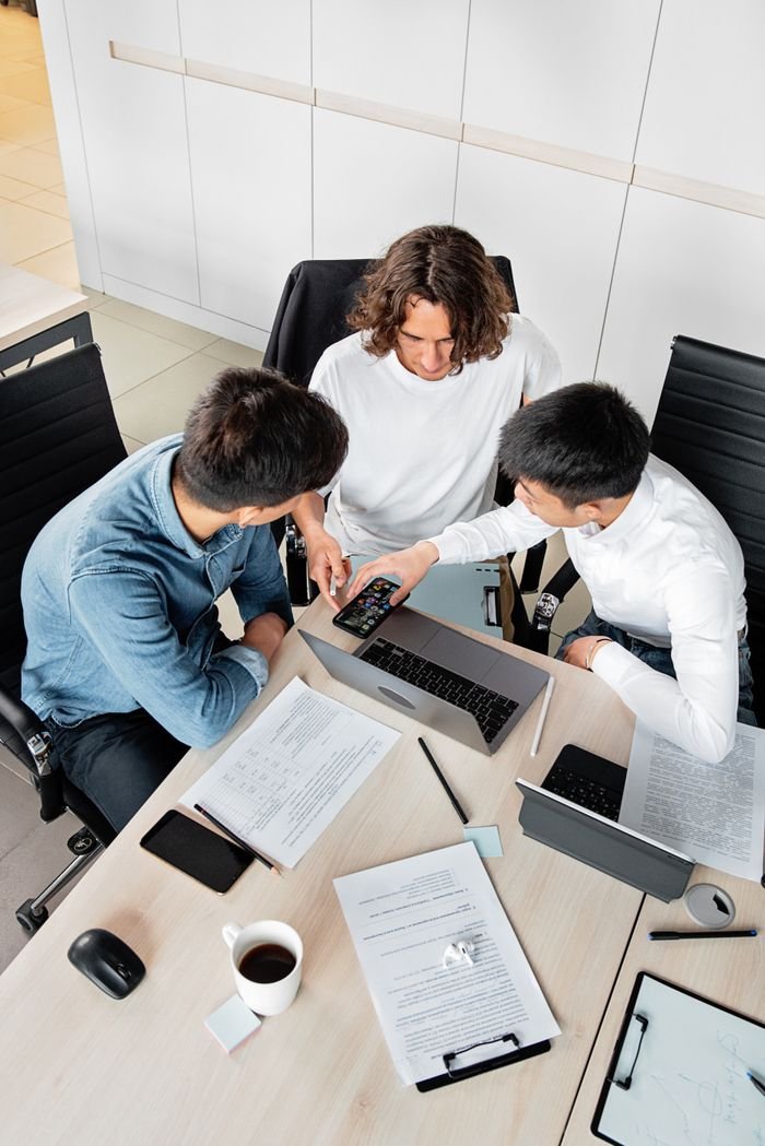 Overhead view of three colleagues collaborating at a desk with laptops and documents.